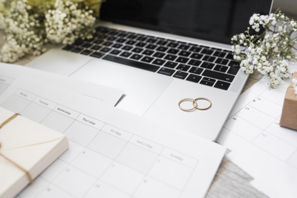 Primer plano del calendario anillos de boda aliento de bebe flores y computadora portatil en el escritorio